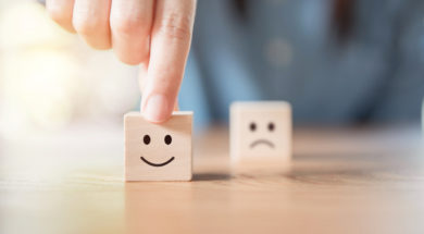 Close up hand choose smiley face and blurred sad face icon on wood cube