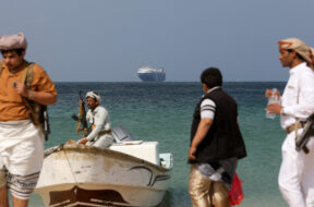 FILE PHOTO: Armed men stand on the beach as the Galaxy Leader commercial ship, seized by Yemen’s Houthis last month, is anchored off the coast of al-Salif